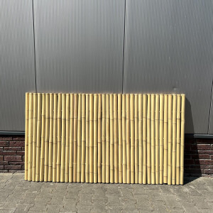 Sichtschutzmatte aus Bambusstäben, 180 cm x 100 cm, vor einer Metallwand platziert. Die Bambusstäbe sind gleichmäßig angeordnet und bieten eine natürliche, dekorative Abgrenzung. Ideal für den Garten oder Terrassenbereich.