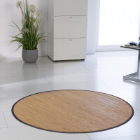 Runder Bambusteppich mit schmaler dunkler Bordüre und feiner Maserung, auf hellem Laminatboden in einem modernen Raum mit weißen Möbeln und einer Pflanze im Hintergrund.
