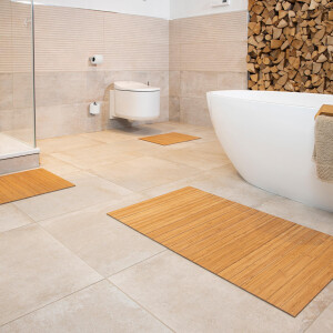 Moderner Badezimmer mit mehreren Bambus Badematten in verschiedenen Größen auf dem hellen Fliesenboden. Die Bambusmatten verleihen dem Raum einen natürlichen und warmen Akzent. Im Hintergrund sind eine freistehende Badewanne und eine Toilette zu sehen.