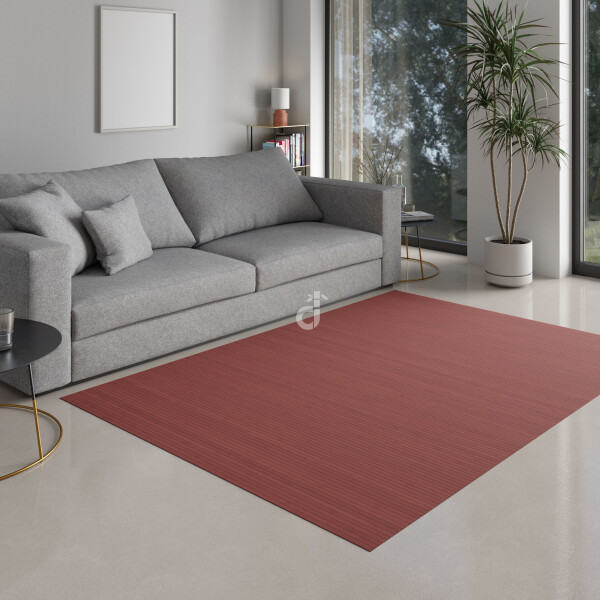 Rechteckiger Bambusteppich in warmem Rotton „Aurora“ mit schmalen Bambusstreifen, platziert vor einem grauen Sofa auf hellem Holzboden in einem modern eingerichteten Wohnzimmer. Oben rechts ist das DE-COmmerce-Logo zu sehen.