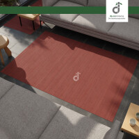 Von oben fotografierter rechteckiger Bambusteppich im warmen Rotton ‚Aurora‘ mit schmalen Bambusstreifen. Der Teppich liegt auf grauen Fliesen zwischen zwei grauen Sofas. Oben rechts ist das DE-COmmerce-Logo.