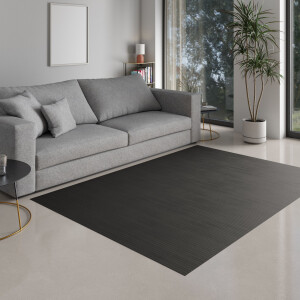 Kind sitzt auf einem großen, dunklen Bambusteppich MASSIVE Wunschmaß steel in einem modernen Wohnzimmer und malt mit Buntstiften auf Papier.