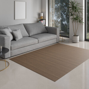 Ein lächelndes Kind sitzt auf einem großen Bambusteppich in Taupe, der auf einem hellen Wohnzimmerboden liegt. Der Teppich hat eine geradlinige, massive Struktur und passt sich harmonisch in die moderne Einrichtung ein.