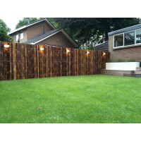 Sichtschutz aus dunklem Bambus, der als Zaun in einem Garten verwendet wird. Die Zaunelemente sind 70 cm breit und 200 cm hoch, bieten Privatsphäre und fügen sich harmonisch in die natürliche Umgebung ein.