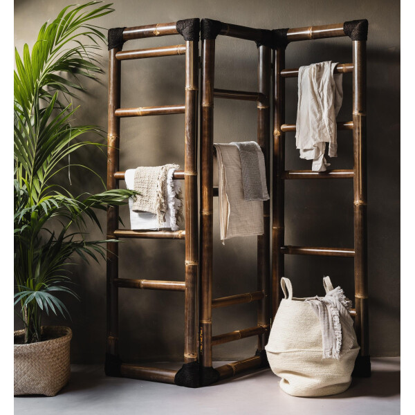 Dekorativer Bambus-Raumteiler SHINTO NIGRA mit drei klappbaren Segmenten, dunkelbraun lackiert. Handtücher und Kleidungsstücke hängen an den Bambusstäben.