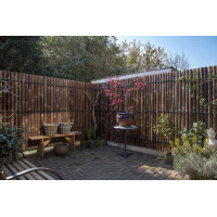 Sichtschutz aus Bambus in Naturfarbe, der als Zaunelement in einem Garten verwendet wird. Die hohen Bambusstäbe bieten Privatsphäre und passen sich harmonisch in das natürliche Umfeld ein.