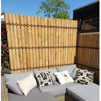 Natürlicher Sichtschutz aus Bambusstäben in heller Farbe, kombiniert mit dunklen Bambusseilen in zickzackförmigem Muster, ergänzt eine helle Outdoor-Sitzecke mit Polstern.