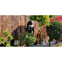 Ein robuster Bambuszaun mit vertikalen Stäben bildet einen natürlichen Sichtschutz im Garten. Die warmen Brauntöne des Bambus harmonieren mit der grünen Bepflanzung und schaffen eine ruhige, asiatisch inspirierte Atmosphäre. Der Zaun ist stabil und bietet Privatsphäre, während er sich elegant in die Gartengestaltung einfügt.