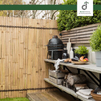 Outdoor-Küchenbereich mit hellem Kisu Bambuszaun („Nature“) im Hintergrund, Arbeitsfläche mit Grill und Küchengeräten, gemütliche Gartenatmosphäre.