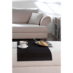 Elegante Couchablage aus dunklem Bambus in der Farbe Ebony, die auf einem hellen Teppich vor einem cremefarbenen Sofa liegt. Auf der Ablage stehen ein Kaffeebecher und ein Teller mit Keksen, was die praktische Nutzung und das stilvolle Design hervorhebt.