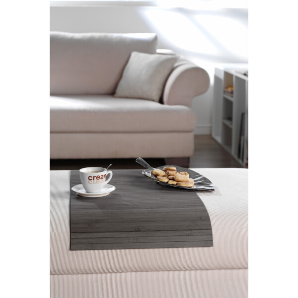 Elegante Couchablage aus Bambus in dunkler Farbe, passend für moderne Wohnzimmer. Mit cremefarbenem Sofa und dekoriertem Tablett mit Keksen und Kaffeebecher.