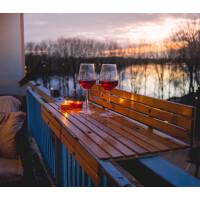 Balkonhängetisch aus Bambus mit zwei Weingläsern und Kerzen bei Sonnenuntergang auf einem Balkon mit Blick auf einen See.