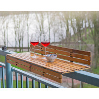 Balkonhängetisch aus Bambus mit zwei Weingläsern und einer Schale, angebracht an einem Geländer mit Blick auf einen grünen Garten.