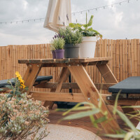 Sichtschutz aus Bambus in natürlicher Farbe, der eine gemütliche Gartensitzecke mit Holzbank und Tisch umgibt. Der Bambuszaun bietet Privatsphäre und schafft eine einladende Atmosphäre im Freien.