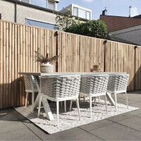 Sichtschutz aus Bambusstäben, die vertikal angeordnet sind, bietet Privatsphäre in einem modernen Garten. Der Bambuszaun ist hinter einem Outdoor-Esstisch mit weißen Stühlen positioniert und schafft eine natürliche, stilvolle Atmosphäre. Ideal für den Einsatz im Freien, um einen geschützten und ästhetischen Rückzugsort zu gestalten.