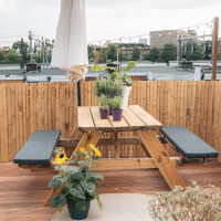 Sichtschutz aus Bambus auf einer Dachterrasse, der eine gemütliche Sitzecke mit Holztisch und -bänken umgibt. Der Bambuszaun bietet Privatsphäre und eine natürliche Atmosphäre.