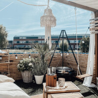 Sichtschutz aus Bambusstäben in natürlicher Optik, Teil einer gemütlichen Gartenlounge mit Lichterketten und Pflanzen, im Hintergrund moderne Gebäude.