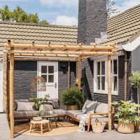 Bambus Pergola NATURE in natürlicher Farbe, die eine gemütliche Sitzecke im Freien überdacht. Die stabile Konstruktion bietet Schatten und verleiht dem Außenbereich ein natürliches, stilvolles Ambiente. Ideal für Garten oder Terrasse, mit komfortabler Lounge-Ecke darunter.