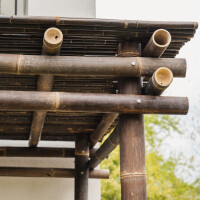 Bambus Pergola NIGRA mit dunklen, stabilen Bambusstangen und einem dichten, natürlichen Dach aus Bambusplatten. Die Konstruktion bietet Schatten und eine gemütliche Atmosphäre im Garten. Maße: 300x300x300 cm (LxBxH).