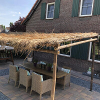 Bambus Pergola NIGRA mit natürlichem Strohdach, die einen rustikalen und gemütlichen Sitzbereich im Freien schafft. Die stabile Konstruktion aus Bambus bietet Schatten und Schutz, ideal für Garten oder Terrasse. Maße: 300x300x300 cm.