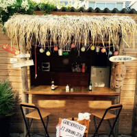 Tiki-Bar mit Strohdach, dekoriert mit Lichterketten und tropischen Elementen, inklusive Holzstühlen und Tresen.