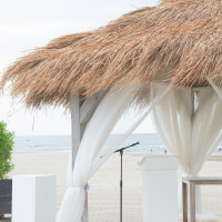 Strandpergola mit Strohdach, Palmdach für Pergolen in den Maßen 200 x 70 cm, aus natürlichen Materialien, mit weißen Vorhängen und Blick auf das Meer.
