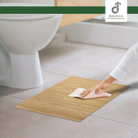 Eine Person reinigt einen Bambus-Badteppich mit einem weißen Tuch in einem modernen Badezimmer. Der Teppich hat ein geradliniges Design mit parallelen Streifen.