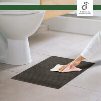 Eine Person reinigt den schwarzen Bambus-Badteppich mit einem Tuch neben einer weißen Toilette. Der Teppich hat eine lineare Struktur und misst 70 x 120 cm.