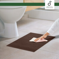 Eine Person wischt mit einem Tuch über den Bambus Badteppich LINES Mocha in der Farbe Mocha, der vor einem Waschbecken und einer Badewanne auf dem Boden liegt.