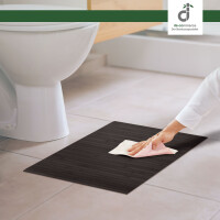 Brauner Bambus-Badteppich mit Linienmuster wird von einer Hand mit einem Tuch gereinigt. Der Teppich liegt vor einem weißen Waschbecken im Badezimmer.