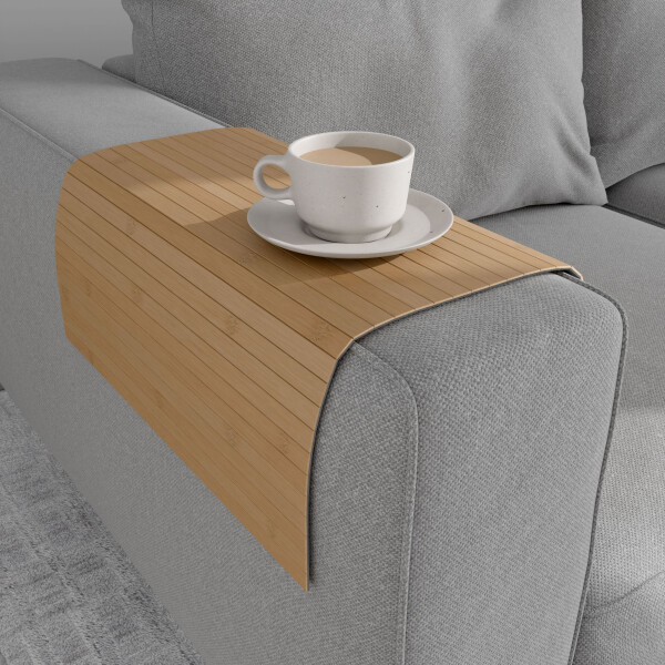 Warmgelbe Bambus-Couchablage mit flexiblen Lamellen liegt über der Armlehne eines grauen Sofas und dient als stabile Ablagefläche für eine Tasse Kaffee auf Untertasse.