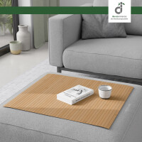 Flexible Couchablage aus Bambus mit Stegstruktur in warmen Gelb mit Braunanteil liegt auf einer grauen Couch und dient als stabile Ablagefläche für Buch und Kerze – ideal als Sofa-Tablett oder Schutz für Polster, oben rechts DE-COmmerce Logo.