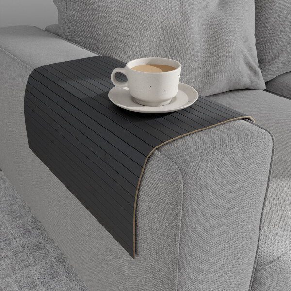 Stahlgraue Bambus-Couchablage mit flexiblen Lamellen liegt über der Armlehne eines grauen Sofas und dient als stabile Ablagefläche für eine Tasse Kaffee auf Untertasse.