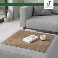 Flexible Couchablage aus Bambus mit Stegstruktur in hellbraun-grau liegt auf einer grauen Couch und dient als stabile Ablagefläche für Buch und Kerze – ideal als Sofa-Tablett oder Schutz für Polster, oben rechts DE-COmmerce Logo.