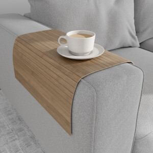 Braungraue Bambus-Couchablage mit flexiblen Lamellen liegt über der Armlehne eines grauen Sofas und dient als stabile Ablagefläche für eine Tasse Kaffee auf Untertasse.