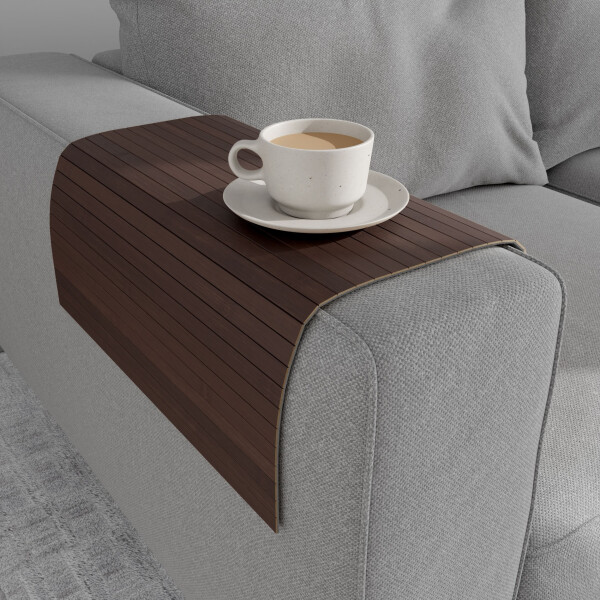 Mittelbraune Bambus-Couchablage mit flexiblen Lamellen liegt über der Armlehne eines grauen Sofas und dient als stabile Ablagefläche für eine Tasse Kaffee auf Untertasse.