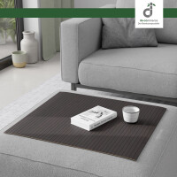 Flexible Couchablage aus Bambus mit Stegstruktur in dunklem Schwarzbraun liegt auf einer grauen Couch und dient als stabile Ablagefläche für Buch und Kerze – ideal als Sofa-Tablett oder Schutz für Polster, oben rechts DE-COmmerce Logo.