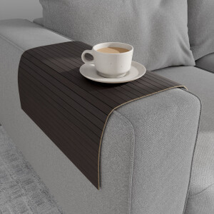Bambus-Couchablage in dunklem schwarzbraun mit flexiblen Lamellen liegt über der Armlehne eines grauen Sofas und dient als stabile Ablagefläche für eine Tasse Kaffee auf Untertasse.