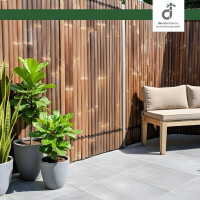 Terrasse mit dunklem Kisu Bambuszaun („Nigra“), Holzbänkchen und Pflanzkübel mit grünen Pflanzen, gemütlicher Außenbereich für Entspannung.