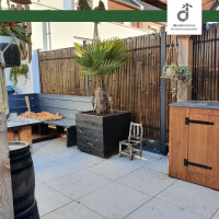 Dunkler Kisu Bambuszaun („Nigra“) auf Terrasse, Sitzbereich mit kleiner Palme in Pflanzkübel, moderner und natürlicher Außenbereich.