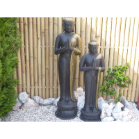 Zwei dunkle Buddha-Statuen stehen vor einem hohen Sichtschutz aus Bambus. Der Bambuszaun hat eine natürliche, vertikale Struktur und passt harmonisch in den Garten mit Steinen und Grünpflanzen.