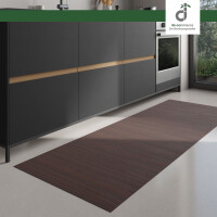 Moderner Küchenbereich mit dunklen Unterschränken und integriertem Backofen; auf dem hellen Boden liegt ein langer, rechteckiger Läufer aus mittelbraunen Bambus. Rechts fällt Tageslicht durch ein großes Fenster ein. Oben rechts ist das DE-COmmerce Logo.