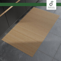 Rechteckiger, hellbrauner Bambusläufer mit feinen Längsstreifen liegt auf einem grauen Steinboden vor modernen, dunklen Küchenunterschränken. Oben rechts befindet sich das DE-COmmerce Logo.