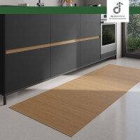 Moderner Küchenbereich mit dunklen Unterschränken und integriertem Backofen; auf dem hellen Boden liegt ein langer, rechteckiger Läufer aus Bambus in einem warmen Gelbton mit Braunanteil. Rechts fällt Tageslicht durch ein großes Fenster ein. Oben rechts ist das DE-COmmerce Logo.