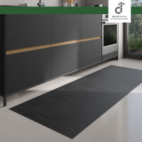 Moderner Küchenbereich mit dunklen Unterschränken und integriertem Backofen; auf dem hellen Boden liegt ein langer, rechteckiger Läufer aus stahlgrauen Bambus. Rechts fällt Tageslicht durch ein großes Fenster ein. Oben rechts ist das DE-COmmerce Logo.