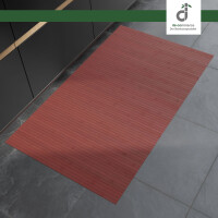 Rechteckiger, roter Bambusläufer mit feinen Längsstreifen liegt auf einem grauen Steinboden vor modernen, dunklen Küchenunterschränken. Oben rechts befindet sich das DE-COmmerce Logo.