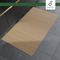 Rechteckiger Bambusläufer in einem hellen Bambuston mit feinen Längsstreifen liegt auf einem grauen Steinboden vor modernen, dunklen Küchenunterschränken. Oben rechts befindet sich das DE-COmmerce Logo.