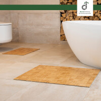 Modernes Badezimmer mit hellen Fliesen, einer freistehenden weißen Badewanne und einer Wandtoilette. Auf dem Boden liegen zwei rechteckige Bambusmatten mit quadratischem Flechtmuster. Im Hintergrund Kaminholz zu sehen. Oben rechts befindet sich das Logo von DE-COmmerce.