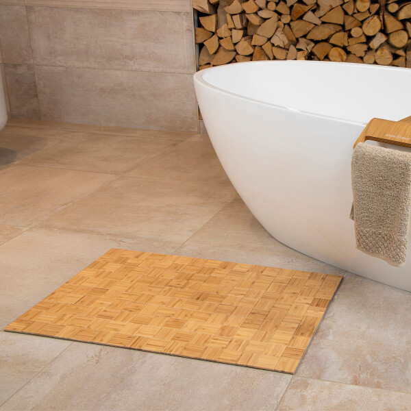 Modernes Badezimmer mit einer freistehenden weißen Badewanne auf hellen Fliesen. Daneben liegt eine rechteckige Bambus-Badematte, und im Hintergrund ist Kaminholz zu sehen. Über den Rand der Badewanne hängt ein beigefarbenes Handtuch.
