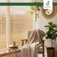 Gemütlicher Sitzbereich mit hellem Sessel und beige Strickdecke, daneben ein kleiner Holztisch mit Tasse und Büchern. Im Hintergrund hängen natürliche Schilfjalousien vor einem großen Fenster, ergänzt durch einen runden Flechtspiegel und mehrere Zimmerpflanzen. Oben rechts befindet sich das DE-COmmerce Logo.